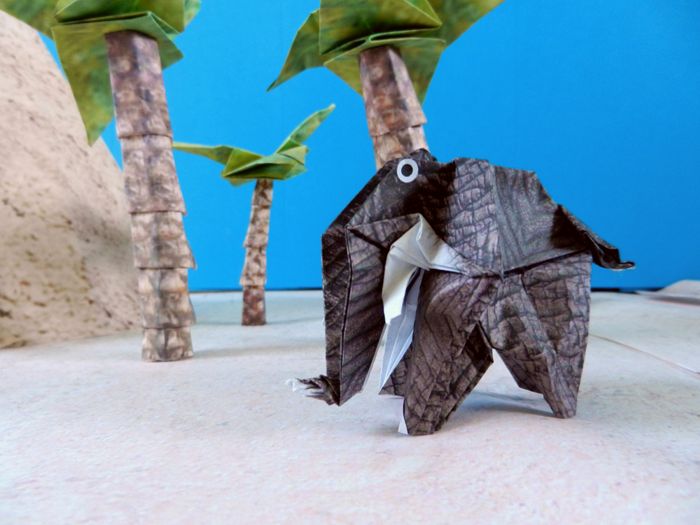 origami elephant in front of two paper palm trees