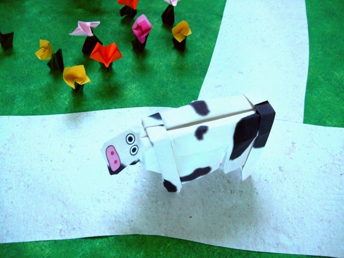 origami cow walking over a path through the land