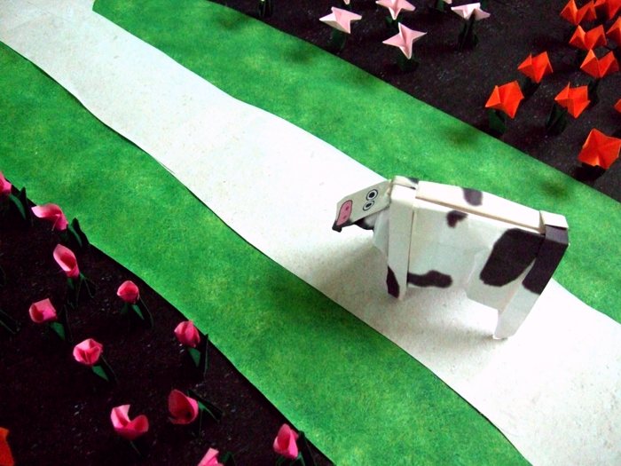 origami cow walking through a large flower field