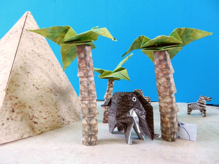 origami elephant resting under large paper palm trees
